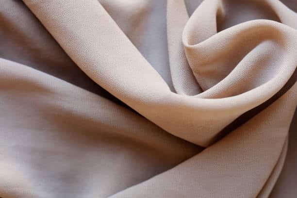Close-up of soft beige chiffon fabric with flowing texture.