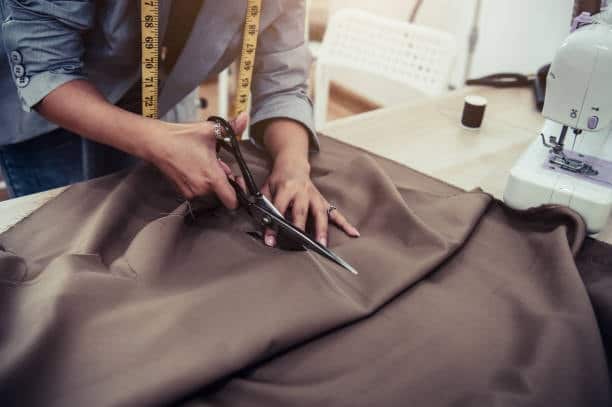 Fashion designer cutting fabric with scissors for custom clothing projects.