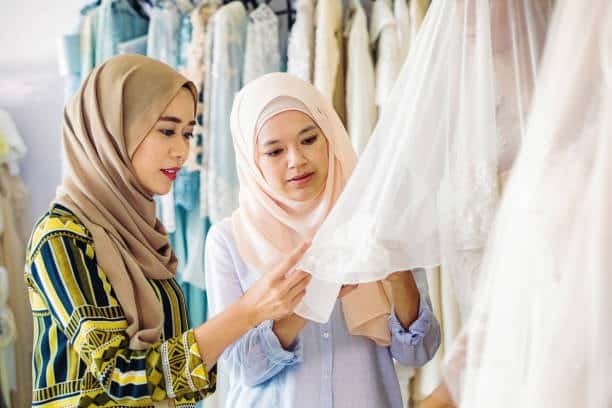 Two women examining a lace wedding dress, showcasing a delicate cloth fabric type used in formal apparel.