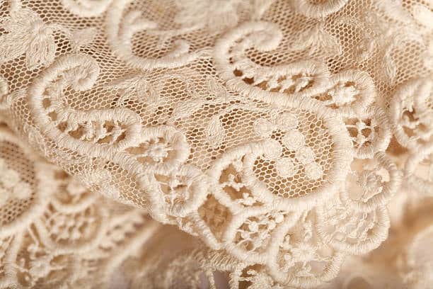 Close-up of delicate beige lace, representing a decorative cloth fabric type used in elegant textile apparel.