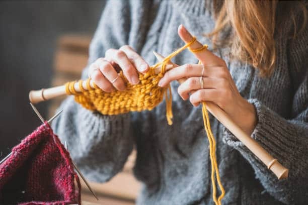 Person knitting a yellow wool sweater, showcasing a natural fiber cloth fabric type for cozy textile apparel.