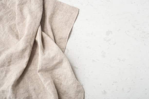 Folded beige linen cloth fabric on a white surface, showcasing a natural fiber textile commonly used in apparel.