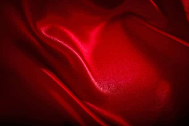 Close-up of flowing red satin fabric, highlighting a smooth synthetic cloth fabric type used in elegant apparel.