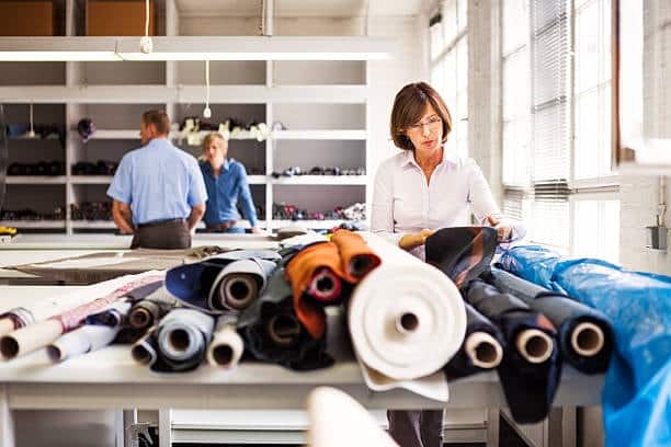 Woman selecting fabric rolls in a textile store for clothing design.