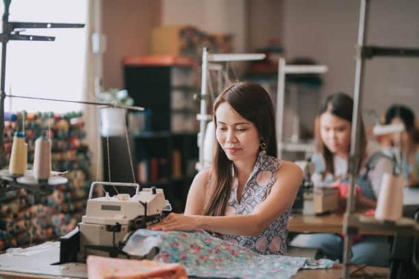 Woman sewing a floral fabric on a machine, demonstrating the use of patterned cloth fabric types in apparel production.