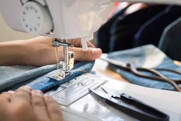 Close-up of a sewing machine stitching denim pants, emphasizing the need for precise yards of fabric to complete the project.