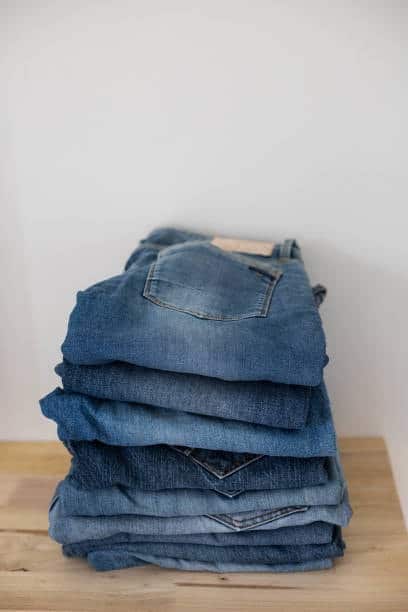 Stack of folded denim pants on a wooden surface, illustrating the importance of calculating yards of fabric for multiple pairs.