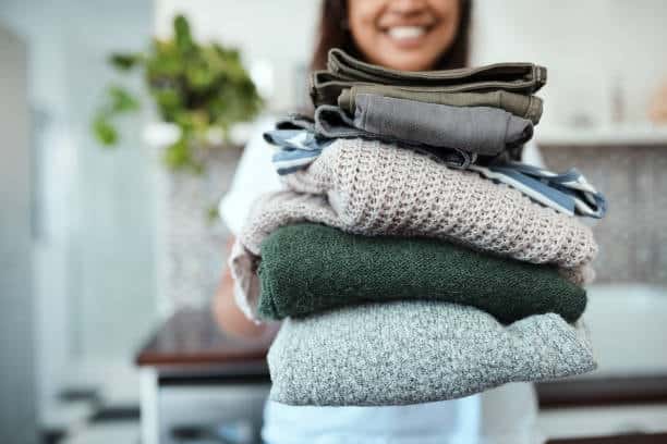 Person holding a stack of wool sweaters and pants, highlighting natural and synthetic cloth fabric types for apparel.