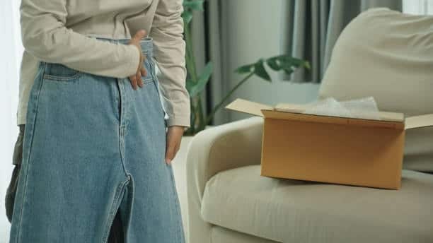 Person trying on blue jeans from a box, highlighting the importance of accurate yards of fabric calculations for a proper fit.