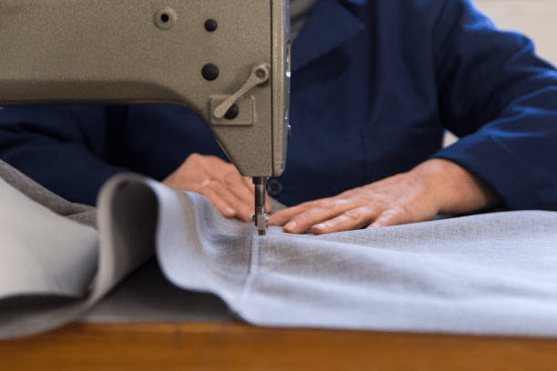 Tailor sewing garment fabric using an industrial machine during final stitching