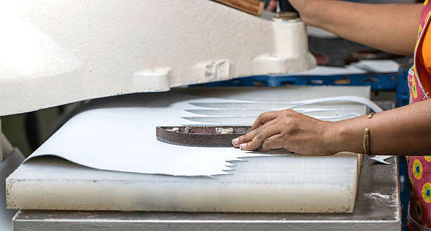 Worker using die cutting machine to shape fabric pieces in apparel manufacturing