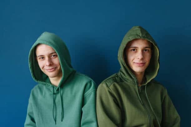 Two young men wearing green hoodies side by side, emphasizing minimalist and casual fashion.
