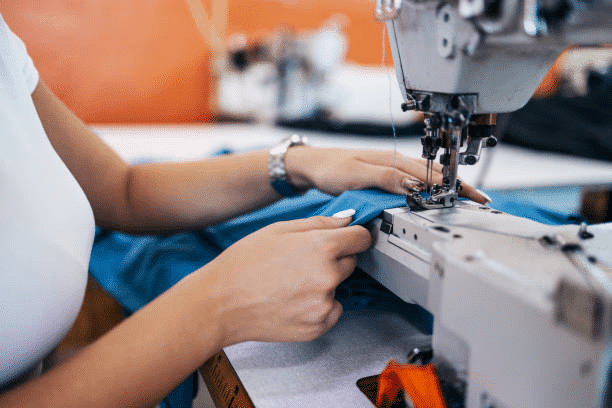 Tailor sewing garment fabric on industrial machine in clothing factory