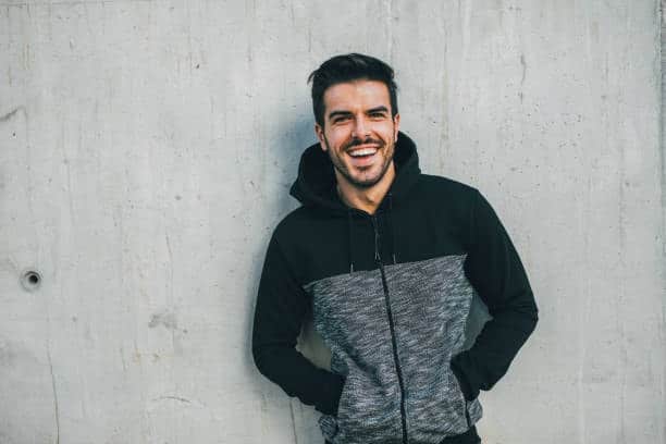 Stylish man wearing a black and grey zip-up hoodie leaning on a wall, showcasing modern men's hoodie fashion
