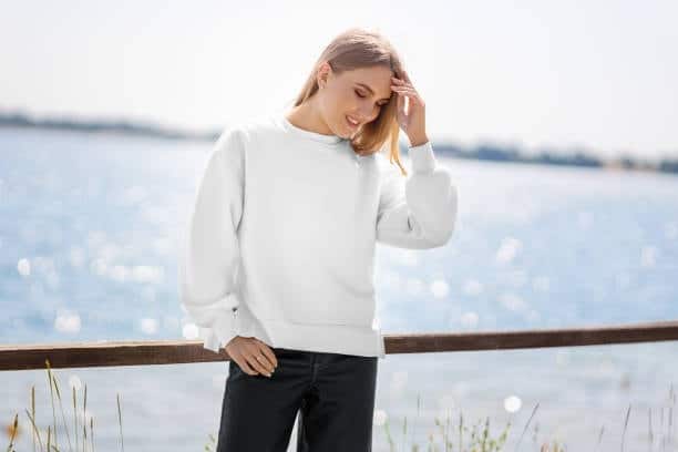 Young woman in a white sweatshirt standing by the water, highlighting clean and casual sweatshirt style