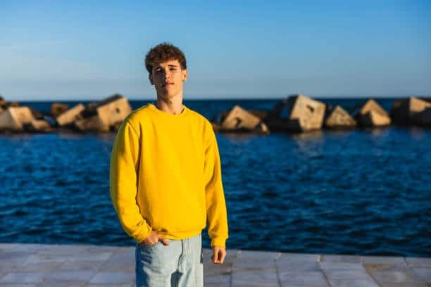 Young man wearing a yellow sweatshirt by the sea, showing vibrant sweatshirt fashion for outdoor settings